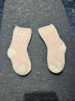 Ljusrosa stickade ullstrumpor - Mysiga ljusrosa stickade strumpor i ull med ribbad struktur och vit tå och häl. Perfekta för kalla dagar när du vill ha det extra varmt om fötterna. Klassisk modell med mjuk känsla och diskret färgton.