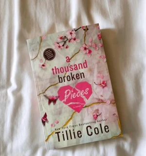 A Thousand Broken Pieces - En gripande roman med ett vackert omslag prytt av körsbärsblommor och ett krossat hjärta. Perfekt för dig som gillar känslostarka berättelser och vill läsa något som berör. Skriven av New York Times-bestsäljande författaren Tillie Cole.