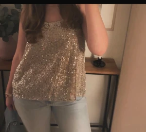 Guldig paljett tubtopp - Säljer en glittrig guldig tubtopp med paljetter som verkligen sticker ut. Har en loose passform, perfekt för dig som vill ha något extra till kvällen. Materialet är syntet och toppen är helt täckt av paljetter för maximal effekt.