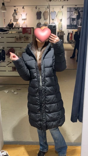 Svart lång varm pufferjacka med huva - Säljer denna långa, svarta pufferjacka från Lager 157 i storlek XS. Den är i bra skick och är otroligt varm under kalla dagar. Det är den populära figursydda modellen med huva som har en smickrande passform. Jackan är praktisk med tvåvägsdragkedja och sidfickor med dragkedja, samt en vattenavvisande yta (Bionic finish® eco). En perfekt och snygg vinterkappa som håller dig varm hela säsongen!