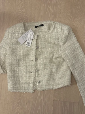 Jacka  - Säljer en snygg vit tweedjacka från Gina Tricot i storlek 36. Jackan har en croppad passform, rund halsringning och silvriga knappar framtill. Materialet är strukturerat och ger en exklusiv känsla. Perfekt för dig som vill ha en trendig och stilren look. Helt ny, pris kan diskuteras 