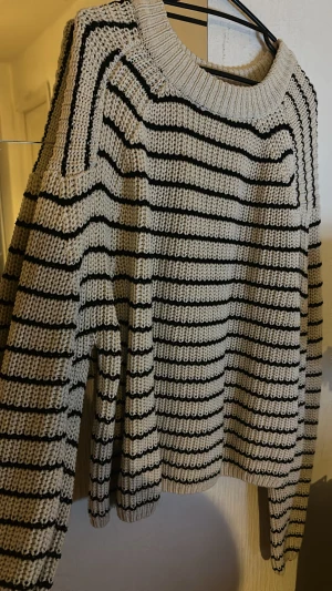 Randig stickad tröja i vit och svart - Säljer en oversized stickad tröja med breda ribbade muddar och rund hals. Tröjan är vit med svarta horisontella ränder och har en loose fit. Perfekt för lager-på-lager och chill höst- eller vinterstil.