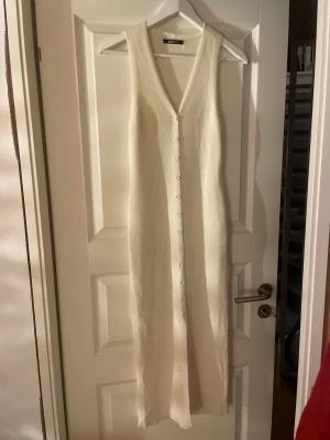 Vit lång stickad klänning Gina Tricot - Lång klänning från Gina Tricot i mjuk vit nyans. Klänningen har v-ringning och knappar hela vägen framtill, vilket ger en clean och stilren look. 