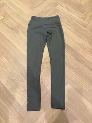 Mörkgrå leggings XS med hög midja - Snygga mörkgrå leggings i storlek XS med hög midja. Tillverkade av 85% nylon och 15% spandex för en stretchig och bekväm passform. Perfekta för träning eller chill dagar, med slät yta och smala ben.