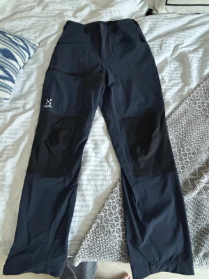 Blå överdragsbyxor från Haglöfs dam 38 - Säljer ett par blå överdragsbyxor från Haglöfs i storlek 38. Byxorna har förstärkta partier på knäna och är tillverkade i slitstark polyamid och polyesterblandning. Perfekta för utomhusaktiviteter som vandring.