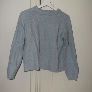 Ljusblå stickad tröja med rund hals - Mysig ljusblå stickad tröja med rund hals och ribbad struktur. Tröjan har långärmade raglanärmar och en enkel, clean design som passar perfekt till jeans eller kjol. Perfekt för kyliga dagar när du vill vara både bekväm och snygg.