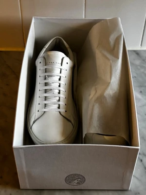 Helt Nya Oliver Cabell vita sneakers - Helt nya, inte använda en ända gång! Snygga vita sneakers från Oliver Cabell, tillverkade i Italien. Skorna har en stilren design med rund tå, platt sula och klassisk snörning. Materialet är mjukt skinn och insidan är fodrad för extra komfort. Perfekta för dig som gillar minimalistisk stil.