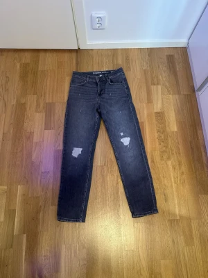 Mörkgrå Garcia Jeans med slitningar - Snygga mörkblå jeans från Garcia Jeans med slitna detaljer på benen och klassisk femficksdesign. Modellen har normal passform och raka ben, med hög midja och dragkedja fram. Perfekt för dig som gillar en cool och avslappnad stil.