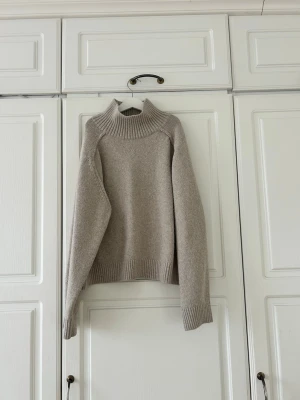 Beige polotröja från H&M, storlek M💖 - Säljer en beige polotröja från H&M i storlek M. Tröjan har en hög, ribbad krage och är stickad med grova muddar vid ärmslut och nederkant. Perfekt för kyliga dagar och har en loose passform som ger en avslappnad vibe.