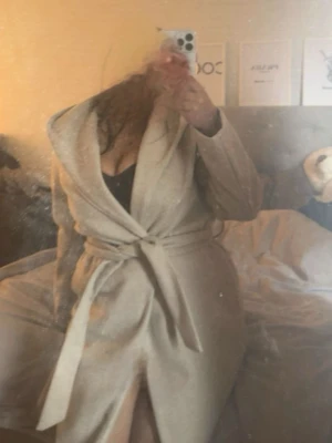 Beige kappa med luva & bälte - Säljer en beige kappa med bälte i midjan och luva. Materialet är mjukt och känns som ullmix. Perfekt för dig som vill ha en clean och chill look. Funkar att ha på vintern då den är tjock material och håller dig varm ⛄️ ❄️ 