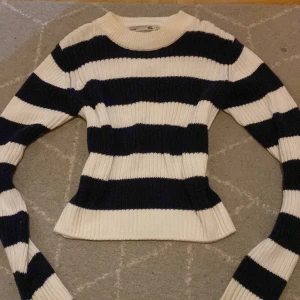 Randig stickad tröja från 157, S - Säljer en ribbstickad tröja från 157 i storlek S. Tröjan har breda marinblå och vita ränder, rund hals och långärmade ärmar. Modellen är figurnära och passar perfekt för dig som gillar klassisk stil med en modern twist.