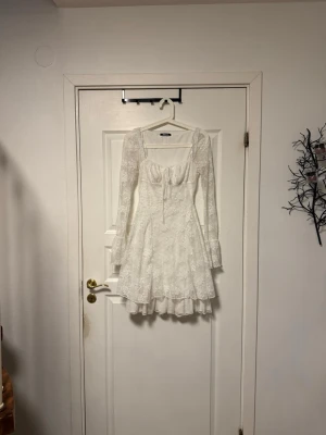 Student klänning, Vit spetsklänning med volang - Superfin vit kortklänning från Gina tricot perfekt till studenten, användning en gång. Från kollektionen 2025 där den har  långärmade spetsärmar och volangkant nedtill. Klänningen har omlottkänsla vid bysten med snörning och ett blommigt spetsmönster över hela tyget.l