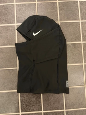 Nike skimask ( helt ny ) fråga om ni vill se hur den sitter  - Säljer en svart balaclava från Nike med vit logga på sidan. Tillverkad i mjukt och stretchigt syntetmaterial som andas. Perfekt för kalla dagar när du vill skydda ansiktet och hålla värmen. Enkel och stilren design.