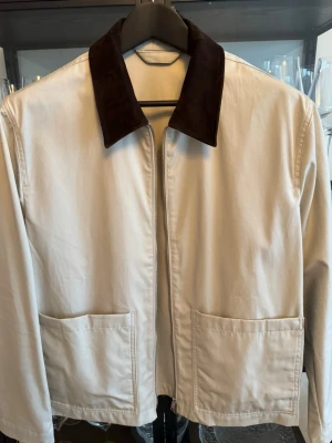 Massimo Dutti Jacka - Snygg beige overshirt med kontrasterande mörkbrun krage och två stora fickor framtill. Jackan har dragkedja och är långärmad, perfekt för lager-på-lager. Materialet känns mjukt och har en clean look som passar till många stilar.
