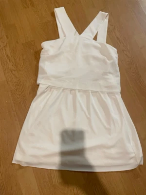 Vit kort klänning från Zara - Snygg vit klänning från Zara med breda korslagda axelband och lätt struktur i tyget. Klänningen är kort och har en enkel, stilren design som ger en fräsch look. Perfekt för dig som gillar minimalistisk stil och vill ha något som sticker ut med detaljerna i ryggen. Priset går att diskutera 