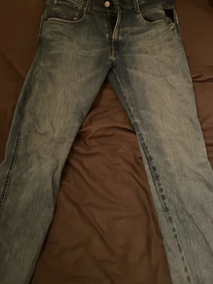 Replay Anbass blå slim jeans, stl W31 L30 - Säljer ett par Replay Anbass jeans i blå tvätt med snyggt slitna detaljer. Modellen är slim fit med klassiska fem fickor, dragkedja och Replay-lapp bak i midjan. Jeansen har ljusa kontrastsömmar och är perfekta för dig som gillar en modern look.