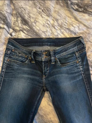 Blå pepe jeans bootcut jeans - Snygga blå jeans från pepe jeans med klassisk bootcut och låg midja. Jeansen har slitningar och detaljerade bakfickor med broderad våg. Materialet är jeans med en skön stretch och de har fransade benslut för en cool vibe.