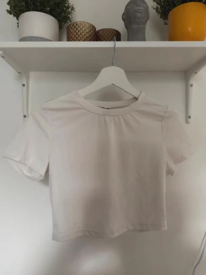 Vit croppad t-shirt - Enkel och stilren vit croppad t-shirt med rund halsringning och korta ärmar. Perfekt att matcha med jeans eller kjol för en clean look. Gjord i mjukt bomullsmaterial som känns skönt mot huden.