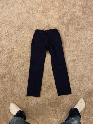 Mörkblå chinos från Holly & Whyte - Snygga mörkblå chinos från Holly & Whyte by Lindex i storlek 146. Klassisk rak passform med knapp och dragkedja framtill, samt sidfickor. Perfekta för dig som gillar stilrena och bekväma byxor med lite dressad känsla.
