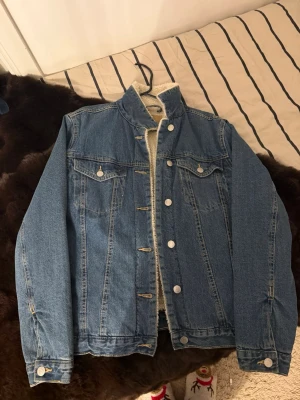 Blå jeansjacka med teddyfoder från 157 - Säljer en blå jeansjacka från 157 med mjukt vitt teddyfoder på insidan och kragen. Jackan har klassisk rak passform, silverfärgade knappar framtill och två bröstfickor med lock. Perfekt för kyliga dagar och riktigt snygg till jeans eller hoodie. Pris kan diskuteras! <3