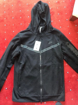 En svart Nike tech med fleece och mjukisbyxor - Säljer ett matchande Nike Tech Fleece-set i svart, bestående av hoodie och byxor i storlek S. Setet är tillverkat i mjukt och bekvämt material med bra passform och stilren design. Lätt att bära både till vardags och för en mer sportig look. I mycket fint skick. Skickas snabbt och pris kan diskuteras vid snabb affär.