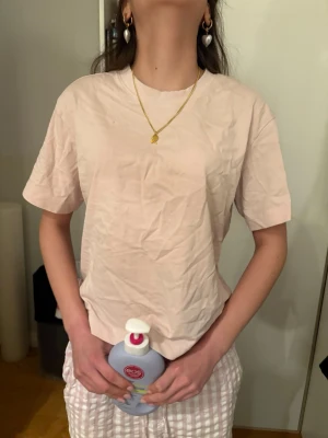 Ljusrosa basic t-shirt i bomull - Säljer en ljusrosa t-shirt med klassisk rund hals och korta ärmar. Modellen är enkel och loose fit, perfekt för en chill och avslappnad stil. Materialet är mjuk bomull som känns skönt mot huden. Passar dig som gillar minimalistiska plagg och softa färger.