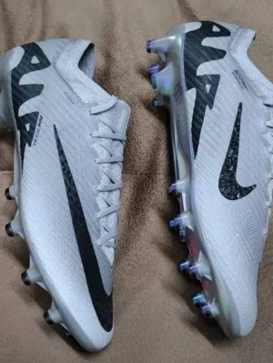 Nike Zoom Mercurial fotbollsskor grå - Nike Zoom Mercurial fotbollsskor i ljusgrå färg med svarta detaljer och stor Swoosh-logga på sidan. Skorna har snörning, platt sula med dobbar och en cool iriserande undersida med rosa inslag. Tillverkade i syntetmaterial för bästa prestanda på planen.