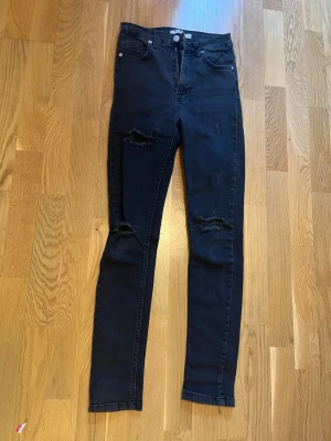 Svarta skinny jeans från NA-KD, strl 36 - Säljer ett par svarta skinny jeans från NA-KD i storlek 36. Jeansen har hög midja, och klassisk femficksdesign. Materialet är stretchigt jeans och de har en snygg, smal passform som sitter tajt längs benen.