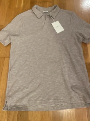 Beige tröja från EastWest - Säljer en beige tröja, t-shirt, från EastWest med klassisk krage och korta ärmar. Toppen är tillverkad i ett mjukt och lätt stickat material som ger en avslappnad känsla. Perfekt för dig som gillar stilrena och neutrala plagg.