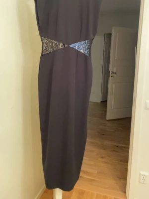 Svart långklänning med spetsdetaljer från Zara - Elegant svart långklänning med spetsdetaljer i midjan som skapar en snygg kontrast. Klänningen har en rak siluett och slits baktill för extra rörelsefrihet. Dragkedja i ryggen för enkel på- och avklädning. Perfekt för dig som gillar stilrena och sofistikerade plagg.