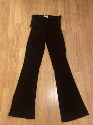 Svarta bootcut yogabyxor från Gina Tricot - Svarta yogabyxor från Gina Tricot i storlek XS. Byxorna har en bred, hög midja och är tillverkade i ett mjukt material som ger en skön känsla. Passformen är loose och benen är utsvängda för en trendig siluett.