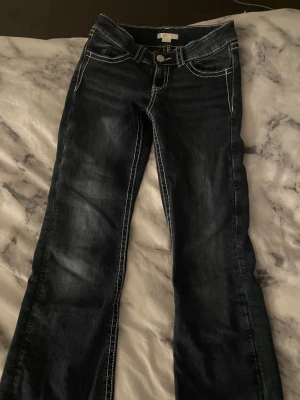 Mörkblå jeans men broderade fickor  - Snygga mörkblå jeans med kontrasterande vita sömmar och detaljerade broderier med paljetter på fickorna Passformen är bootcut  och de är låg midja