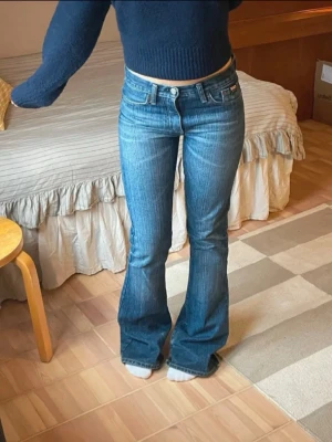 Vintage lågmidjade bootcut jeans - Säljer ett par vintage jeans i blå tvätt med bootcut passform. Jeansen har låg midja, fem fickor och tydliga Levi's detaljer som patch och röd etikett bak. Materialet är slitstarkt denim i bomull och de har en snygg faded look. Lite slitna längst ner