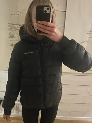 Svart pufferjacka Peak Performance S - Säljer en svart pufferjacka från Peak Performance i storlek S. Modellen heter Tomic Insulated Hood Jacket Dam. Jackan har huva, dragkedja framtill och två sidofickor med dragkedja. Den är vadderad och har en logga på bröstet. Väldigt sparsamt använd och därmed i mycket bra skick utan defekter. 