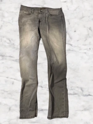 Grå Replay Anbass jeans - Säljer ett par grå Replay Anbass jeans med klassisk femficksdesign och diskret tvättad look. Jeansen har raka ben och normal passform, med Replay-logga på bakfickan. Materialet är slitstarkt jeans och färgen är en snygg mörkgrå ton. Storleken är 34W och 31L men sitter mer som 32-33W. Kan framställas som lite ”pösigare” än normala nudie byxor men dom ser fortfarande riktig snygga ut och dom är även knappt änvända. Bara att höra av sig vid frågor och funderingar.