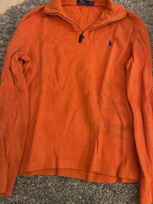 Orange manchestertröja Polo Ralph Lauren - Säljer en orange långärmad tröja från Polo Ralph Lauren i manchestertyg. Tröjan har half zip med metall-dragkedja och klassisk blå logga broderad på bröstet. Perfekt för dig som gillar färg och vill ha en chill stil.