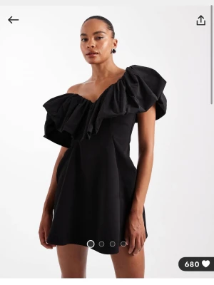 Svart enaxlad miniklänning ASOS DESIGN - Svart, enaxlad miniklänning från ASOS DESIGN med strukturerad passform och stor, skrynklad volang längs halsringningen. Klänningen är sydd i taffeta och har en cool, asymmetrisk look som verkligen sticker ut. Kostar 929 ny!