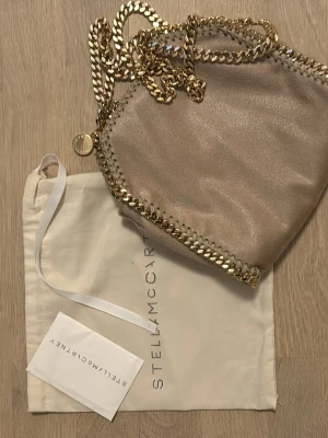 Beige/rosa från Stella McCartney - Säljer en snygg beige/rosa väska  från Stella McCartney med guld kedja. Använd väldigt lite  oxh ser nästan helt oanvänd ut. 