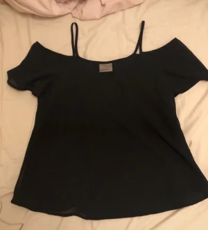 Svart offshoulder topp Vero Moda XS - Svart offshoulder topp från Vero Moda i storlek XS. Tunn och luftig med smala axelband och korta ärmar som sitter snyggt nedanför axlarna. Perfekt för dig som gillar enkel och stilren design med en modern touch.