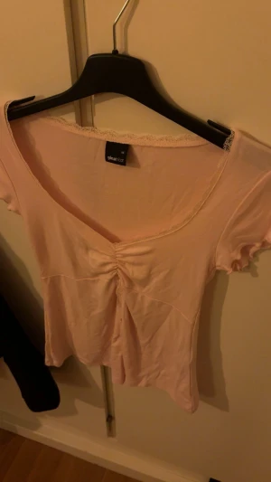 Ljusrosa v-ringad topp från Gina Tricot - Supersöt ljusrosa topp från Gina Tricot i mjuk bomull. V-ringad med spetskant runt halsen. Har aldrig använt den 