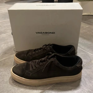 Bruna sneakers från Vagabond - Bruna sneakers från Vagabond med en stilren design. Skorna har en vit, beige sula och är tillverkade i mocka. Storleken är 42 men den är stor i storlek så skulle nog säga 43-44 ungefär. De har snörning för en bra passform och en bekväm innersula. Skorna kostar ny pris 1400kr men jag säljer dom för 400kr pga det finns något lite märke eller skav på skorna. Använt skick. Om ni har några frågor så är det bara att fråga!😉😉