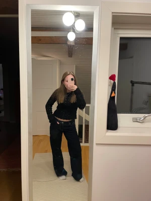 Svart stickad croppad tröja - Svart stickad tröja med lång ärm och croppad passform. Tröjan har ett hålmönster och vågig kant nertill för en snygg detalj. Perfekt till jeans eller kjol för en chill och trendig look.