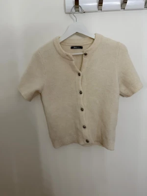 Beige kortärmad kofta Gina Tricot XS - Superfin beige kofta från Gina Tricot i storlek XS. Den har korta ärmar, rund hals och snygga knappar framtill. Mjuk och bekväm, perfekt för höst och vår då den inte är för varm eller kall!