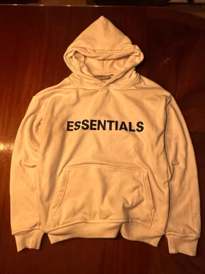 Vit Essentials hoodie  - Den har några märken där fram och på ryggen och lite knopprig, därav priset. Varm och skön nu till vintern. Har du fler frågar är det bara att skicka 🙂