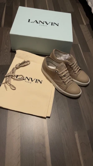 Lanvin skor  - Snygga beige sneakers från Lanvin med klassisk rund tå och platt sula. Skorna har snörning och är tillverkade i en mix av skinn och textil. Kommer med originalkartong, dustbag och extra skosnören. Perfekta för en clean och stilren look. Byter!