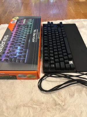 Apex Pro TKL - SteelSeries Apex Pro TKL gamingtangentbord med justerbara Omnipoint-switchar och RGB-belysning. Kommer med handledsstöd och originalkartong. En tangent saknas, annars i gott skick och fullt fungerande. Perfekt för e-sport och gaming.