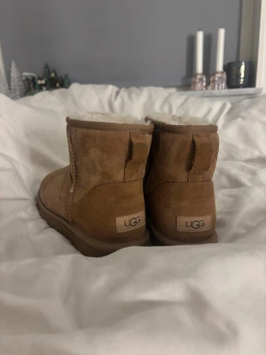 UGG Classic bruna boots med fårskinn - Köp nu så skickar jag den imorgon!!🩷Säljer ett par UGG Classic boots i brun mocka med mjukt vitt fårskinnsfoder. Säljer billigt eftersom dem har vattenfläckar som går att ta bort. Har använts ca 4 gånger!!❄️⛄️Skorna har rund tå, platt sula och UGG-logga bak på hälen. Perfekta för kalla dagar med sin fluffiga insida och slitstarka yttersula.