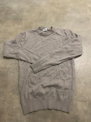 Beige stickad tröja John Henric S - Snygg beige stickad tröja från John Henric i storlek S. Tröjan har rund hals, ribbade muddar och långärmad design. Perfekt för dig som gillar stilrena och enkla plagg med mjuk känsla. Passar dig som vill ha en klassisk look. Det är storlek S men den är liten i storleken 