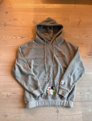 Gallery Dept Hoodie - Säljer en grå hoodie från Gallery Dept. med feta färgstänk, huva med snörning, magficka och tryck på bröstet. Storleken är S men den sitter mer som en M-L. Skicket är väldigt bra och kontakta gärna om frågor om varan eller priset uppstår. 🚚Jag skickar snabbt! 🚚