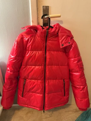 Röd pufferjacka från Moncler - Säljer en riktigt snygg röd pufferjacka från Moncler med glansig finish och huva. Jackan har dragkedja framtill, två fickor med dragkedja och quiltad design. Perfekt för dig som vill sticka ut med en färgstark look under kalla dagar. Köptes begagnad för 5000kr därav priset